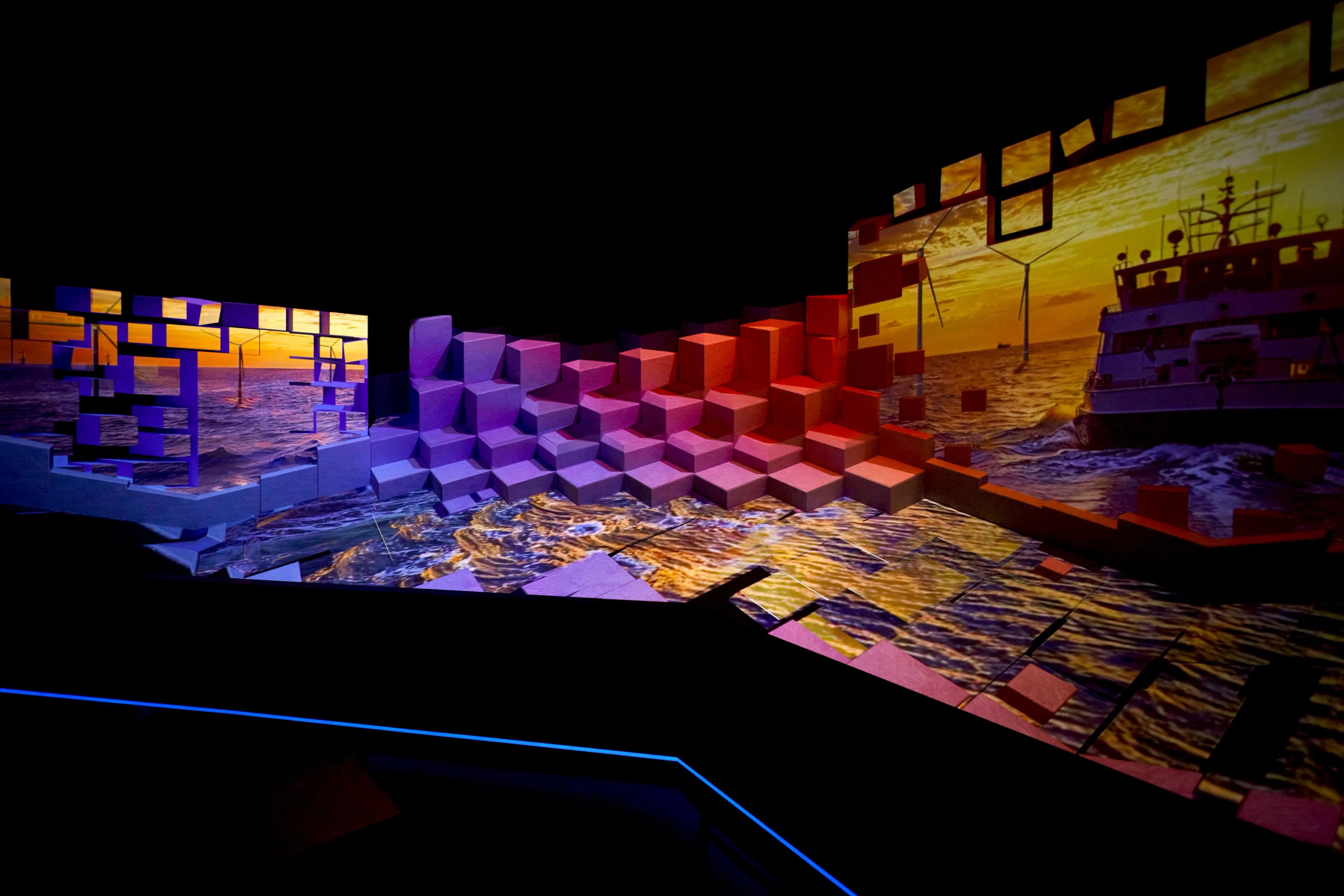 Colorful projection mapping onto a complex structure made of stacked cubes, showing ocean scenes with a ship and wind turbines at the UK Pavilion, Expo 2025 Osaka
